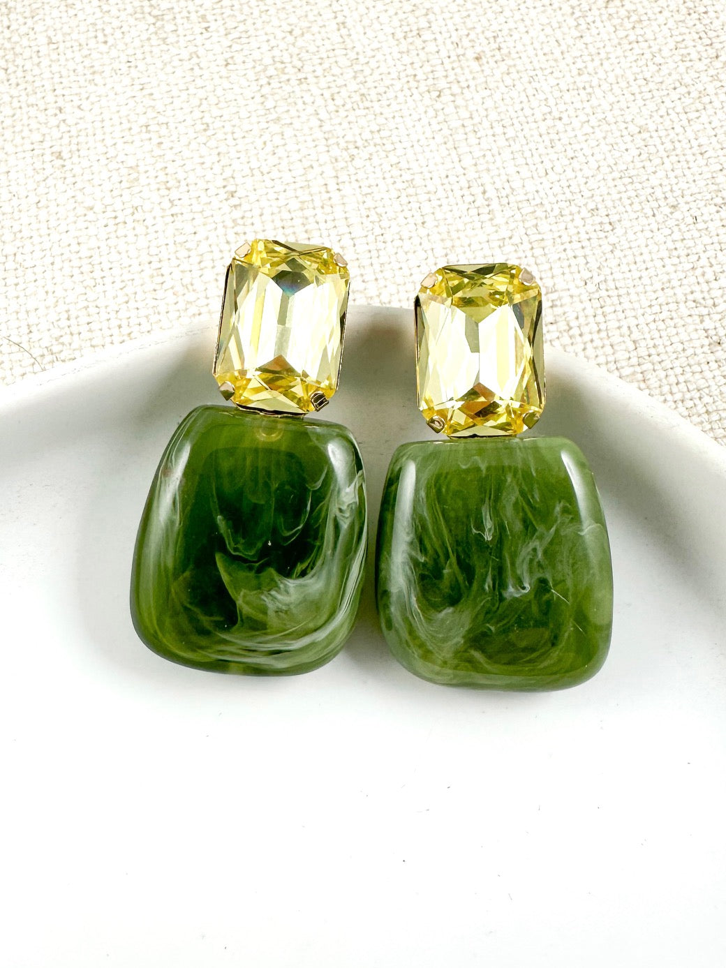Drop earrings with a glossy marbled olive green lower piece and a faceted yellow gem-style top on a light background.
