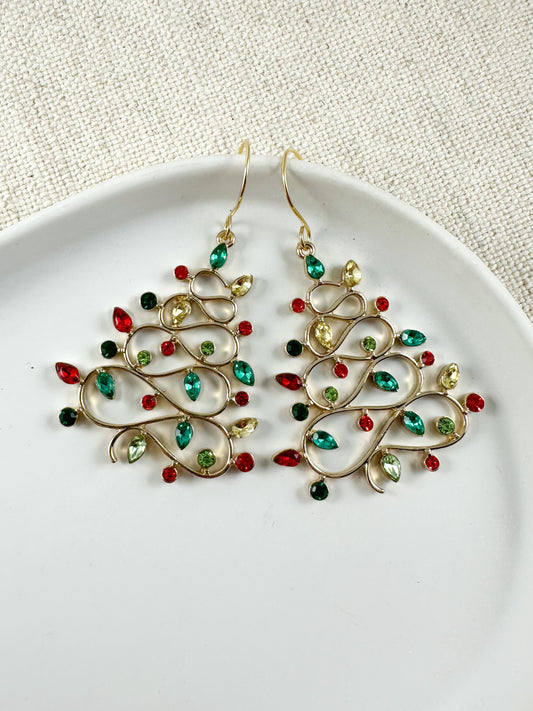 A pair of gold-colored earrings with red and green crystal embellishments, displayed on a white plate against a textured background.