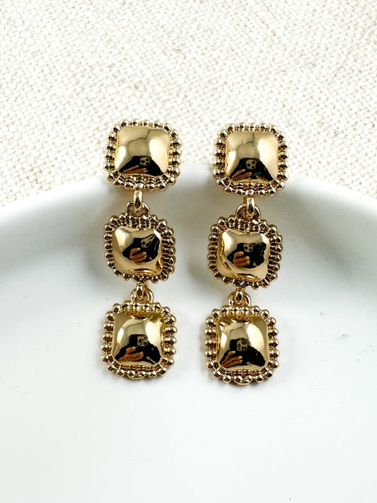 Triple gold square drop earrings with beaded trim shown on white plate background