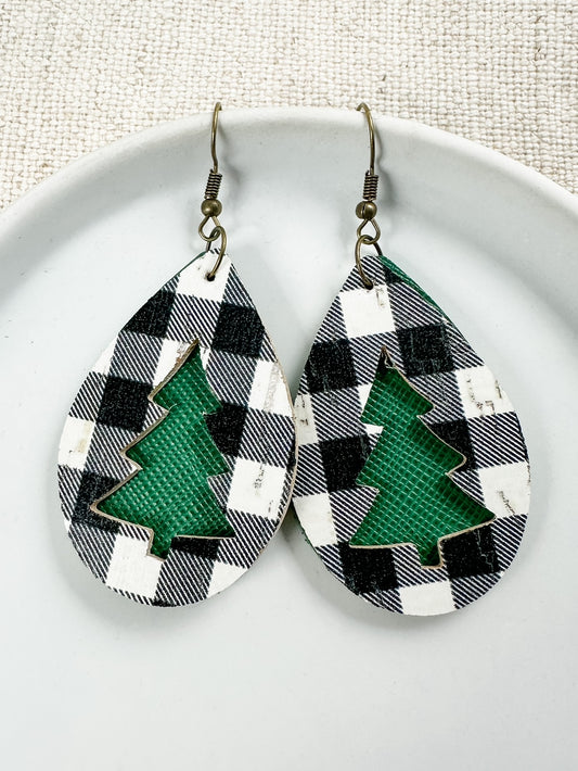 A pair of earrings featuring a black and white checkered pattern with a green Christmas tree cutout, displayed on a white plate.