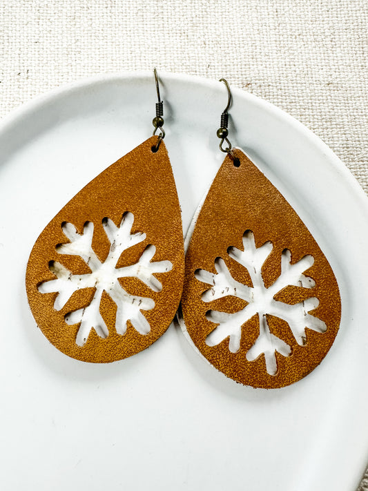 A pair of brown amber-colored earrings with a white snowflake cutout design, displayed on a white plate with a textured background.
