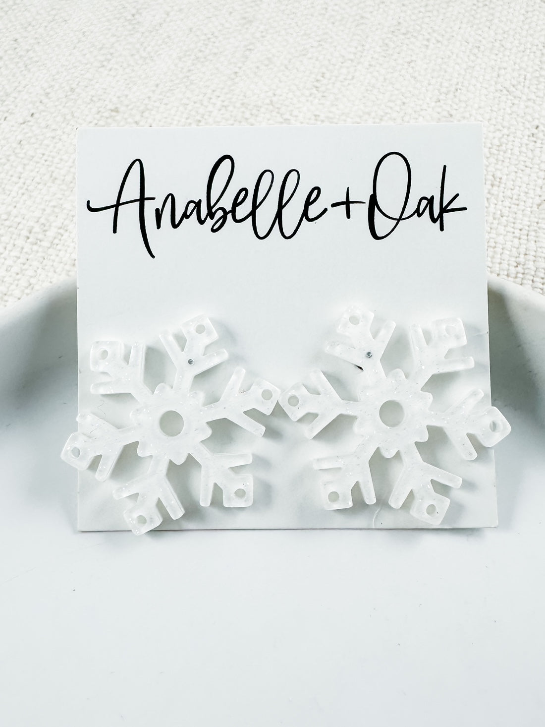 White acrylic snowflake stud earrings with subtle glitter finish, 1" total length, festive winter statement studs from Anabelle+Oak — lightweight and perfect for holiday wear.