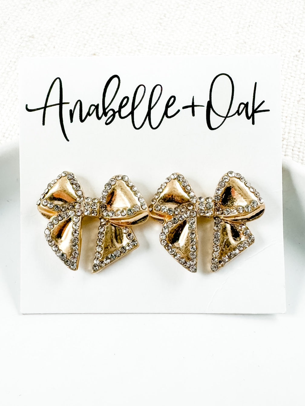 gold bow stud earrings with rhinestone edging shown on a jewelry card