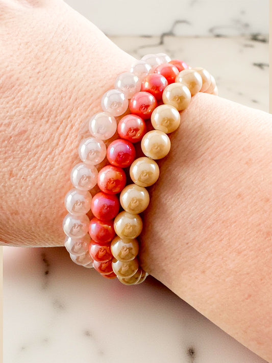 Set of three pearlescent ombré beaded stretch bracelets in soft neutral, coral, and champagne tones stacked on wrist — Golden Hour Bracelet Set from Anabelle+Oak, high-quality layered beaded bracelets for spring, summer, and fall outfits.