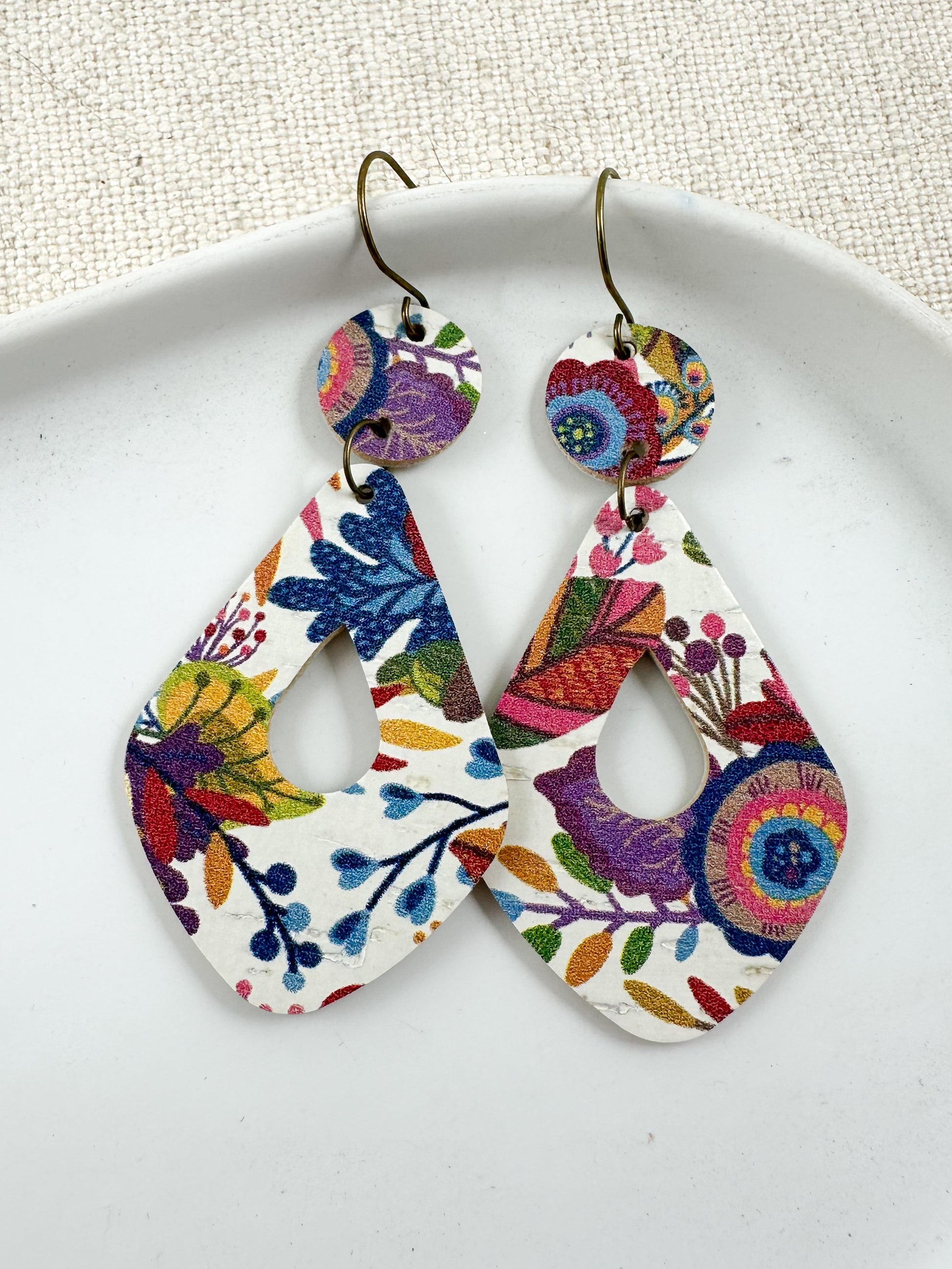 Pair of handmade teardrop earrings in the Briar shape, crafted from genuine cork and leather with a colorful fall floral pattern, displayed on a white dish.