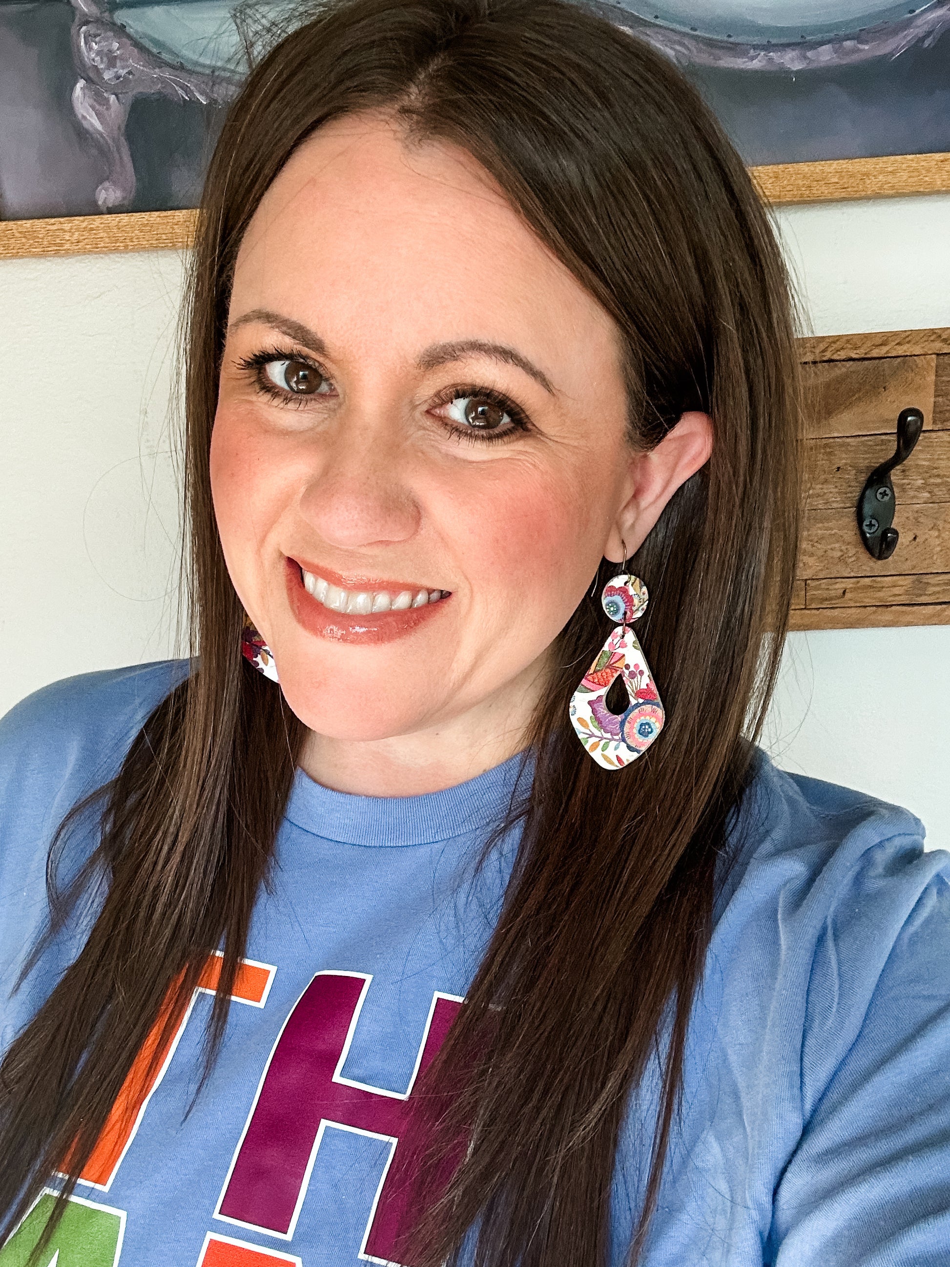 Woman smiling and wearing colorful floral teardrop earrings made from genuine cork and leather, paired with a blue “THANKFUL” long-sleeve tee. The photo highlights the earrings’ lightweight fall floral design.