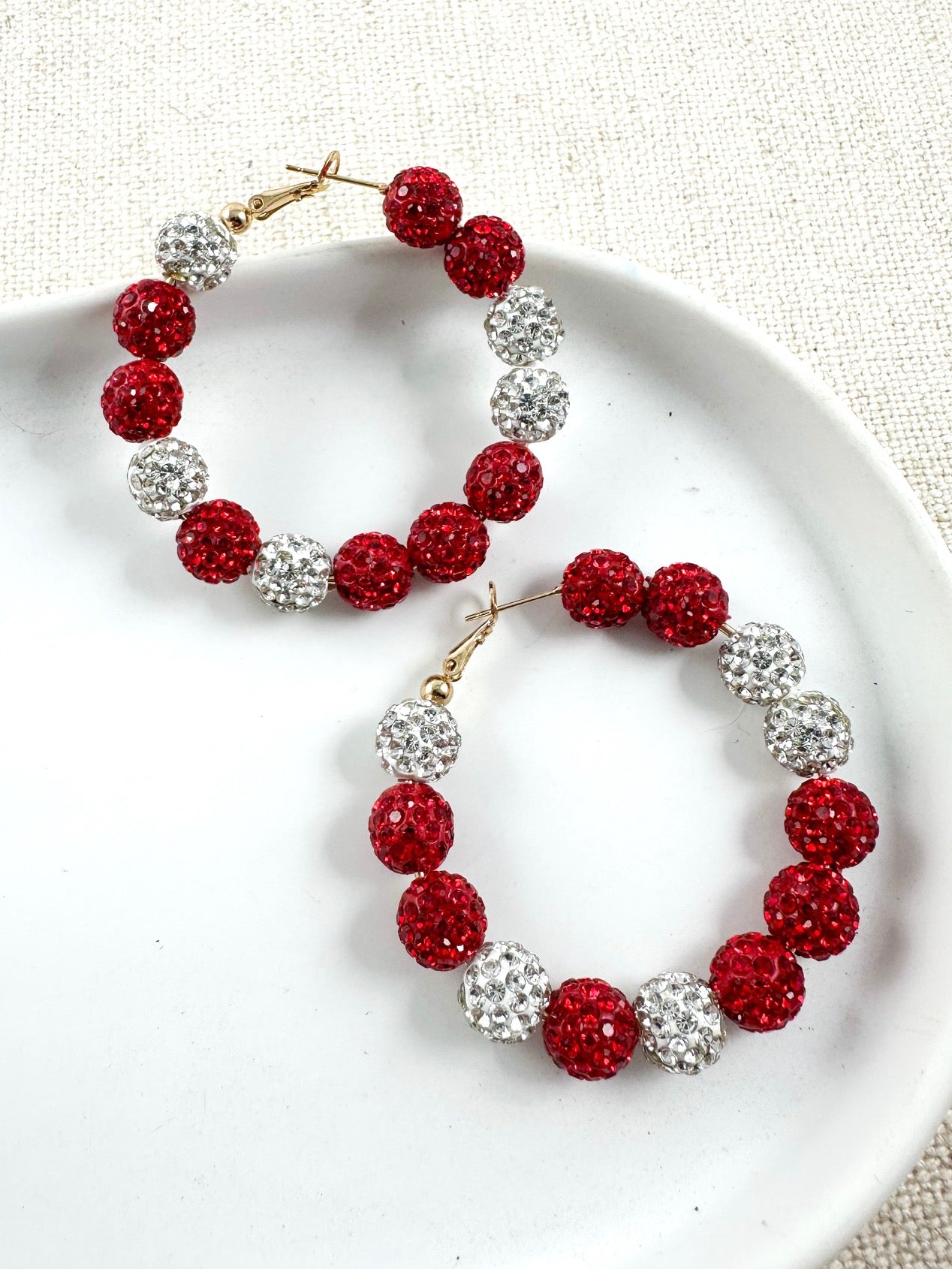 Pair of red and silver sparkle pavé hoops with gold-tone closure shown on white surface