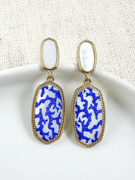 Blue and white Mediterranean-style drop earrings with gold trim and mother-of-pearl tops shown on plate background
