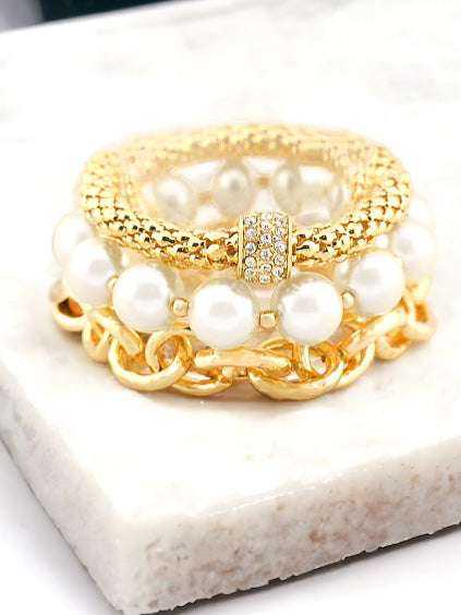 gold and pearl multi-piece bracelet set displayed on a marble jewelry block