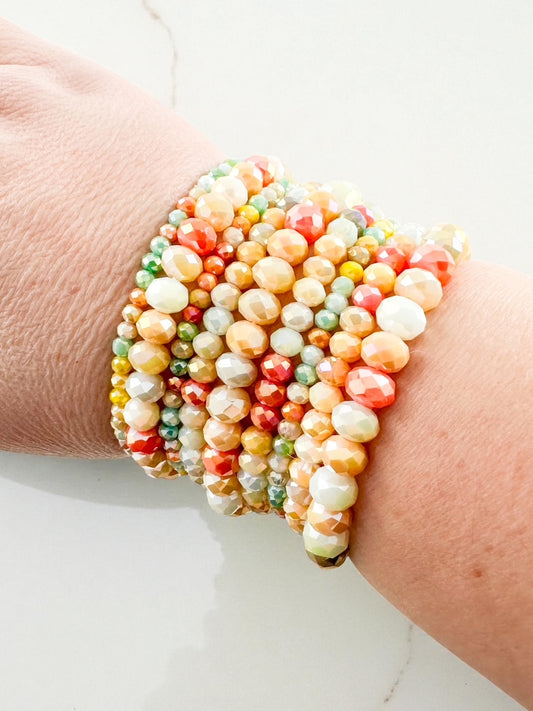 Nine-piece coral and mint beaded bracelet stack with faceted glass beads shown on wrist, featuring multicolor shimmer and layered boho style