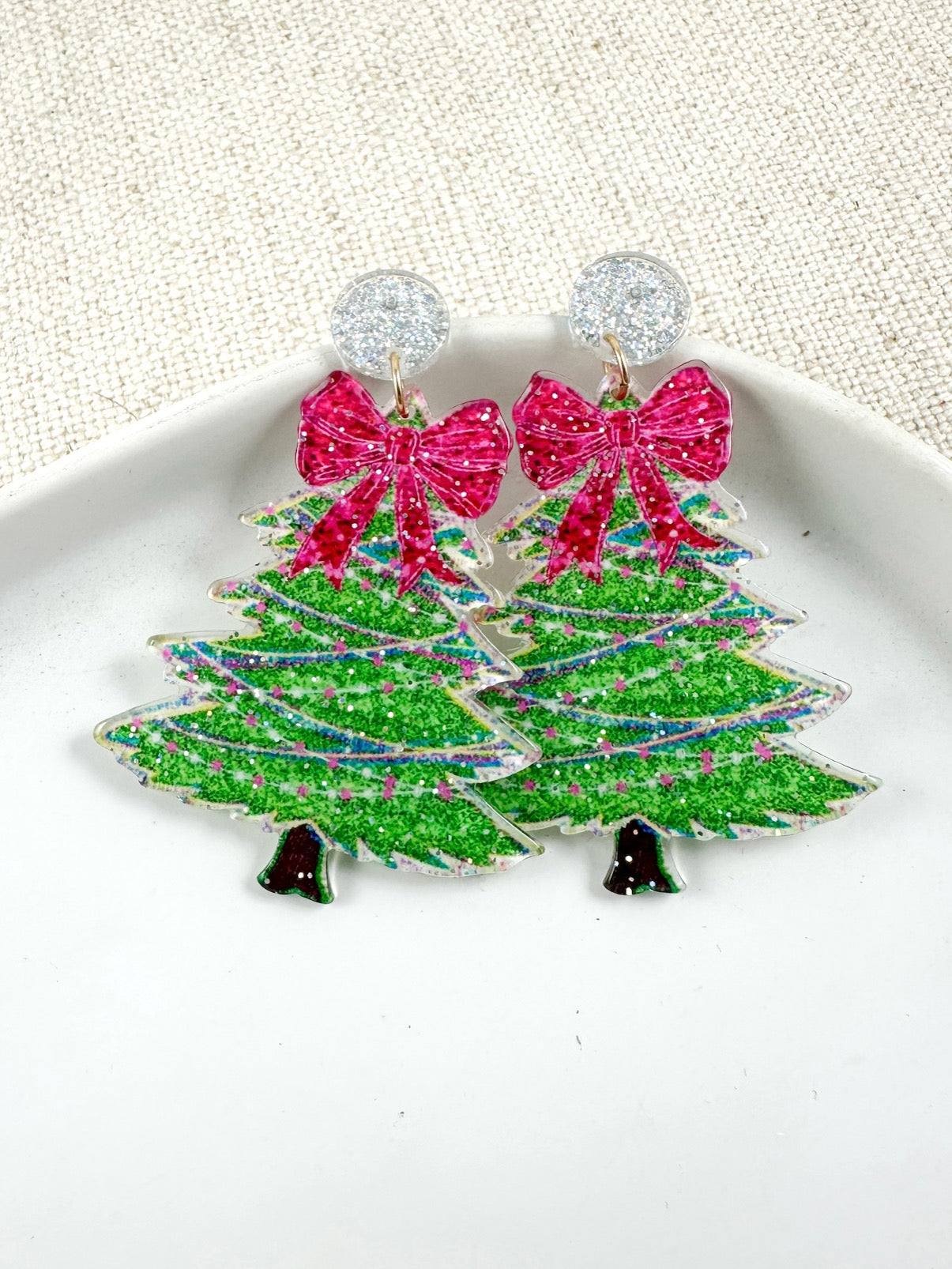 Acrylic evergreen-shaped drop earrings with ribbon detail on a light background