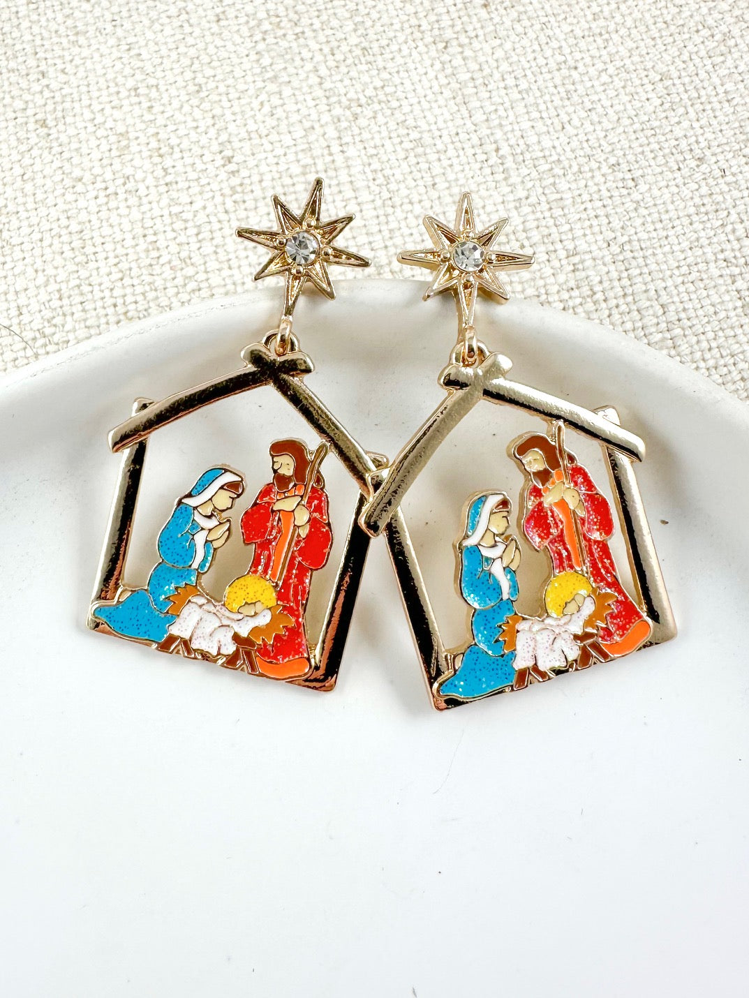 Starlit Nativity Earrings with gold nativity scene charms and crystal-accent star tops on a light background.