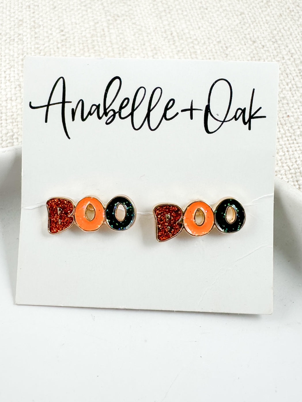 Close-up of Boo Crew Stud earrings with orange, black, and red glitter enamel on white Anabelle+Oak card