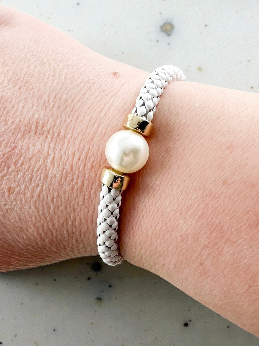 White woven mesh stretch bracelet with a single pearl center bead and gold metal spacer accents shown worn on a wrist.