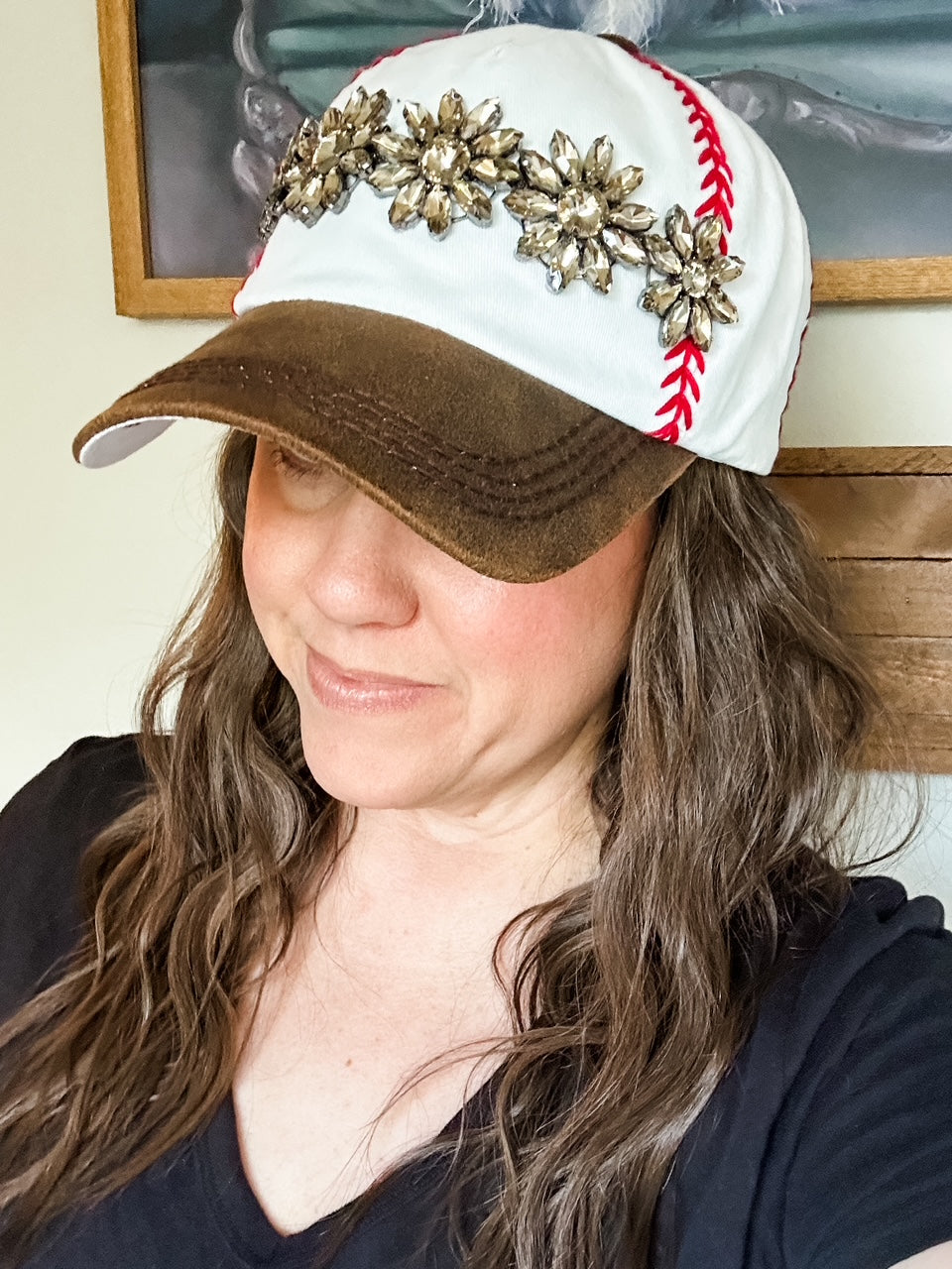 Woman wearing white baseball cap with red embroidered stitching, distressed brown bill, and topaz stone embellishment.