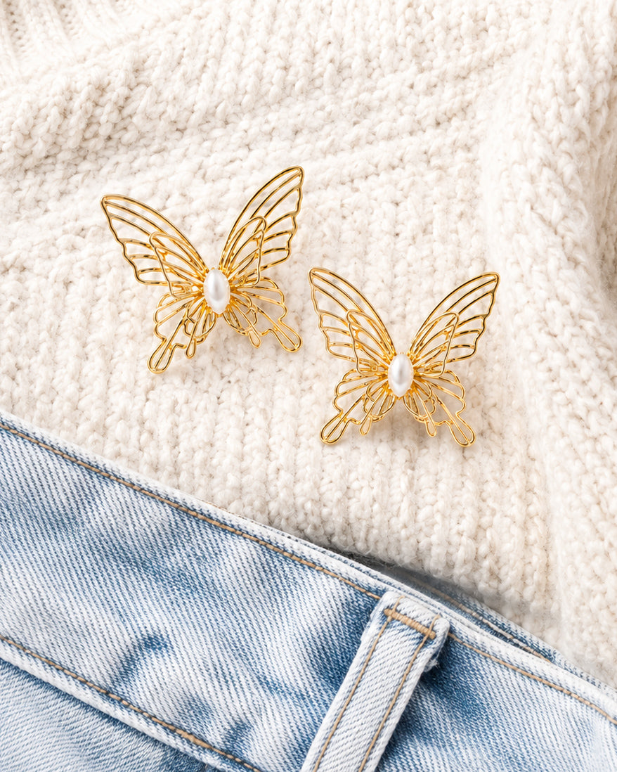 Gold butterfly stud earrings styled with an ivory knit sweater and light wash denim.
