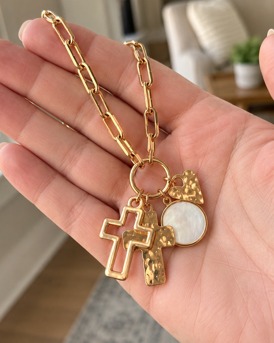 Heart & Soul Necklace held in a hand to show the size of the gold paperclip chain and dangling cross, heart, and pearly charms.