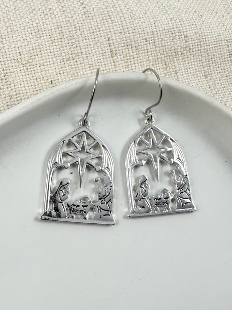 Silver nativity scene earrings with star detail displayed on a white plate