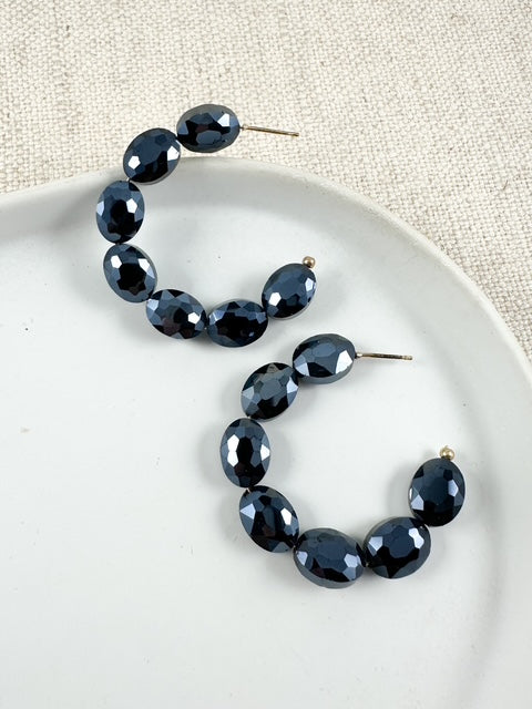 Chunky faceted bead hoop earrings in gunmetal with prismatic dark metallic beads displayed on a white plate