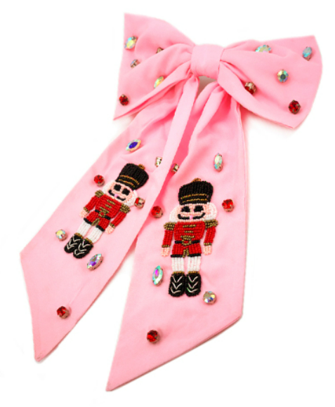 Large pink fabric bow with beaded Nutcracker figures and multicolored gemstone embellishments displayed on a white background