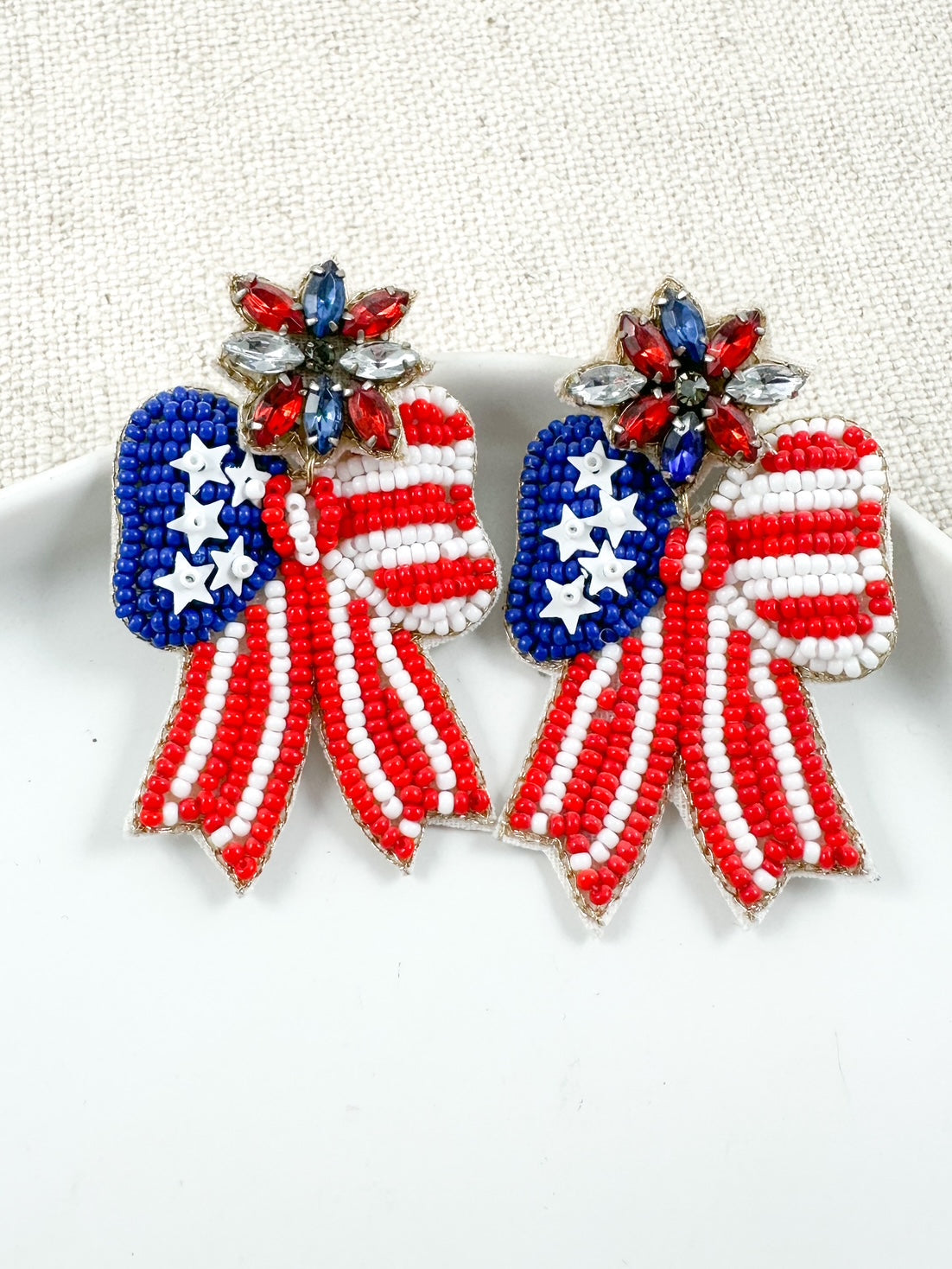 Patriotic Bow Earrings with seed bead and rhinestone details styled in a white ceramic jewelry dish.