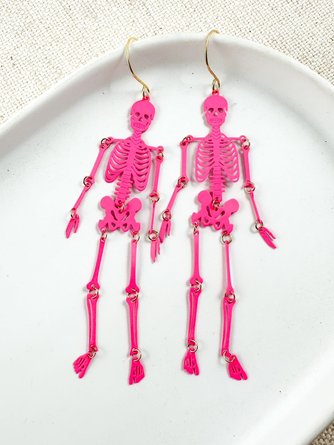 Bright pink skeleton filigree earrings with gold hooks on a white dish