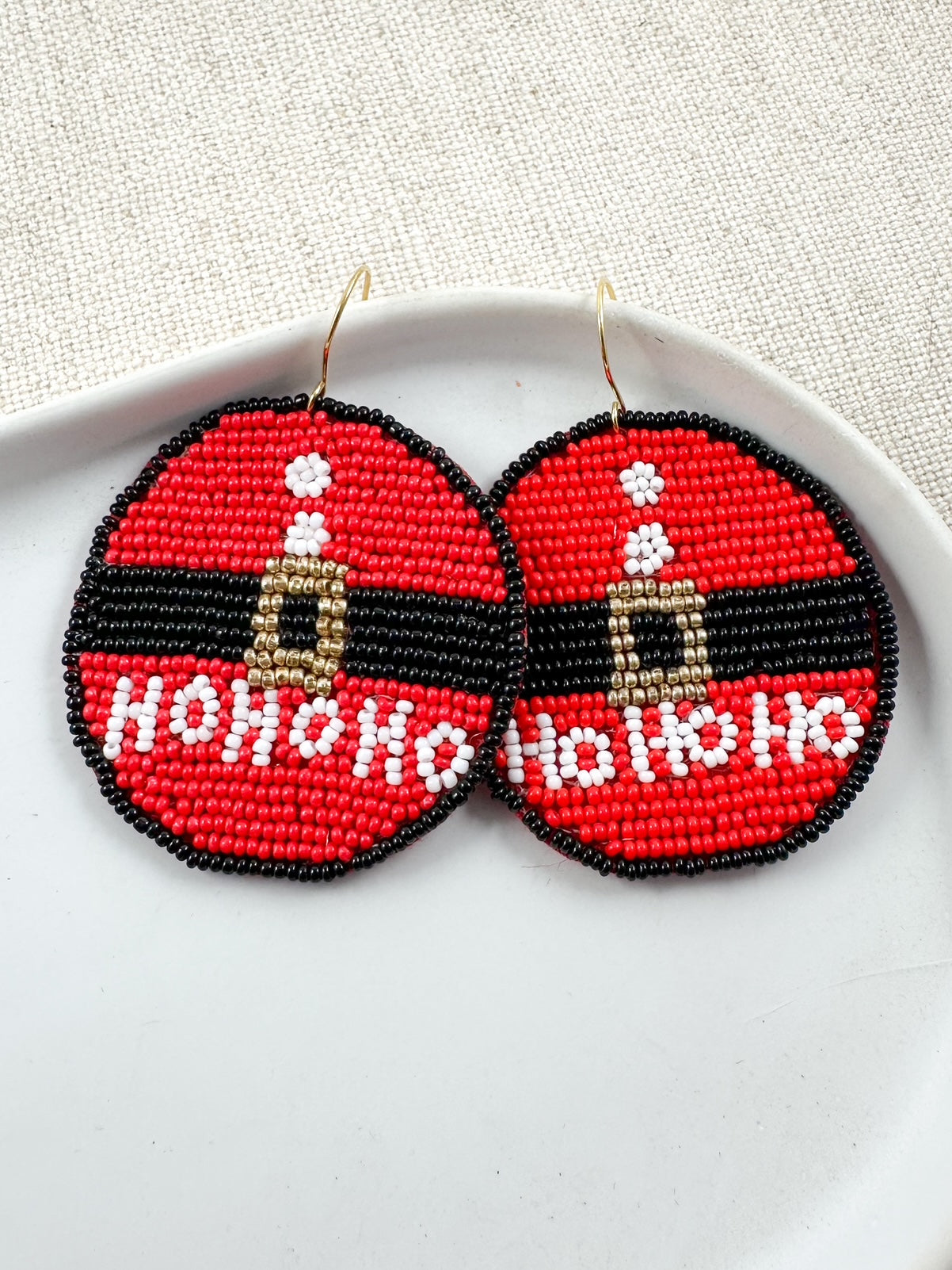 Beaded Santa suit earrings with HO HO HO detail displayed on a white dish.