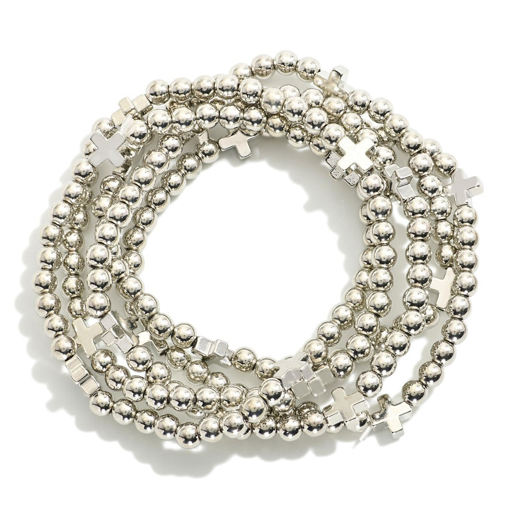 Five silver tone stretch bead bracelets with cross station details arranged in a circular stack on a neutral background.