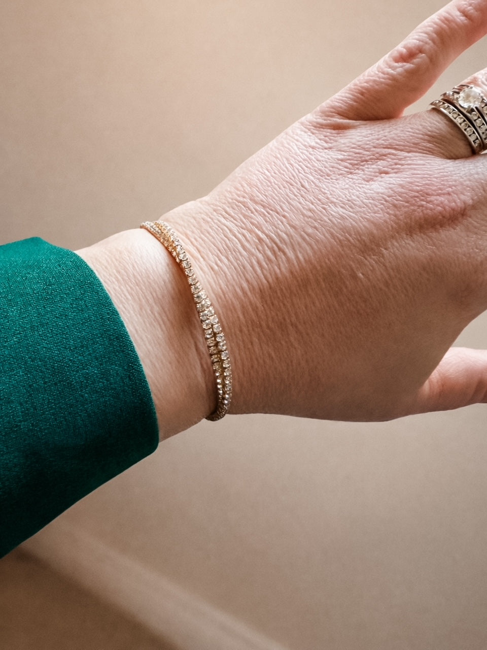 Hand wearing a gold bracelet on a neutral background