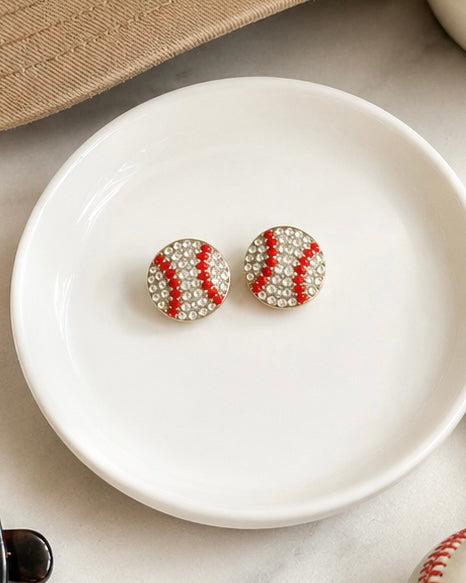 Baseball and softball stud earrings styled with a neutral hat, sunglasses, and baseball for a game day-inspired look.
