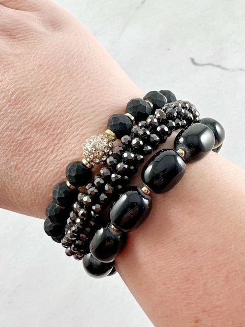 Three black beaded stretch bracelets with faceted and smooth beads stacked on a wrist.