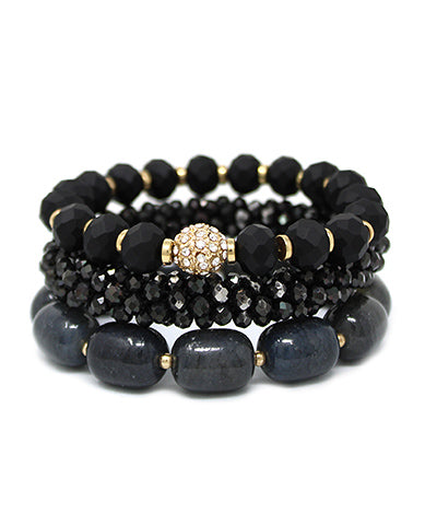 Stack of three black bead bracelets with gold accents laid flat to show details
