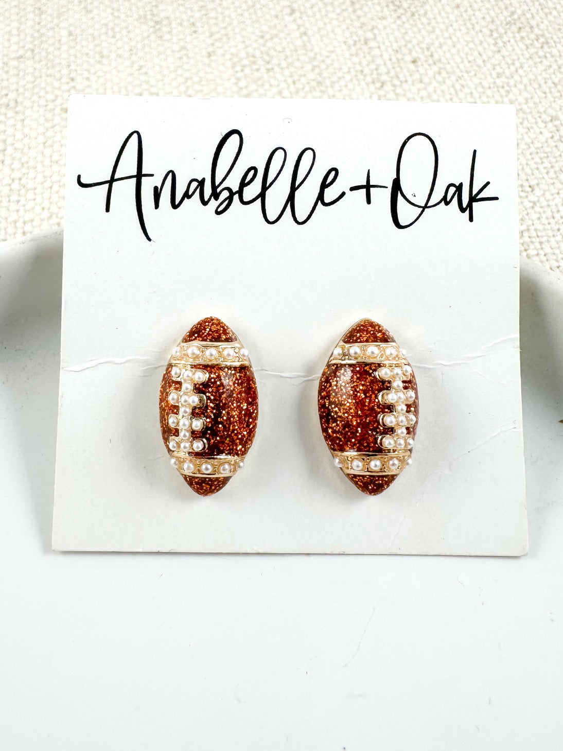 Bronze glitter football stud earrings with pearl detailing on a light background.