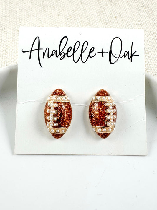 Bronze glitter football stud earrings with pearl detailing on a light background.