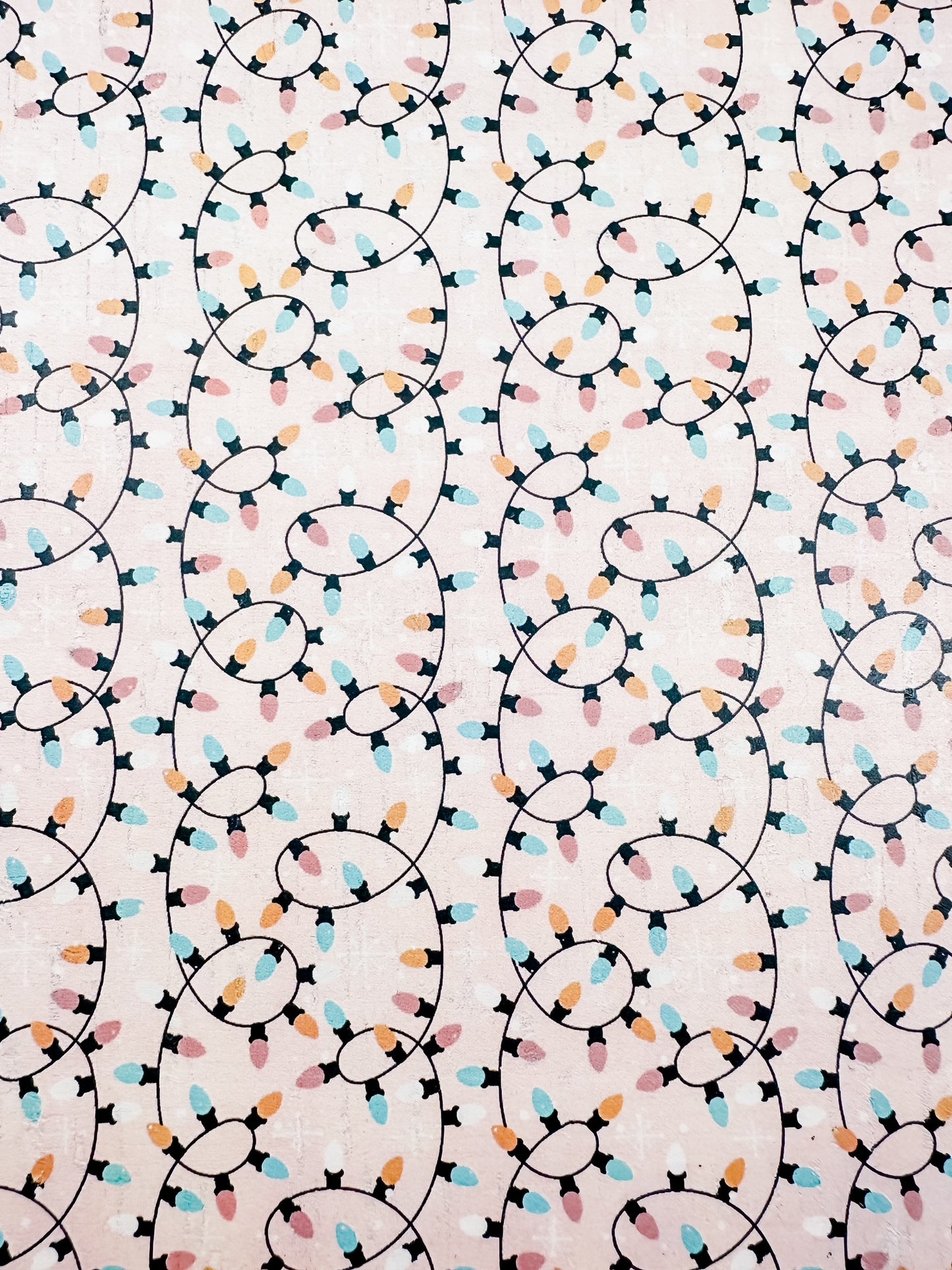 Close-up of blush cork printed with looping strings of pastel Christmas lights