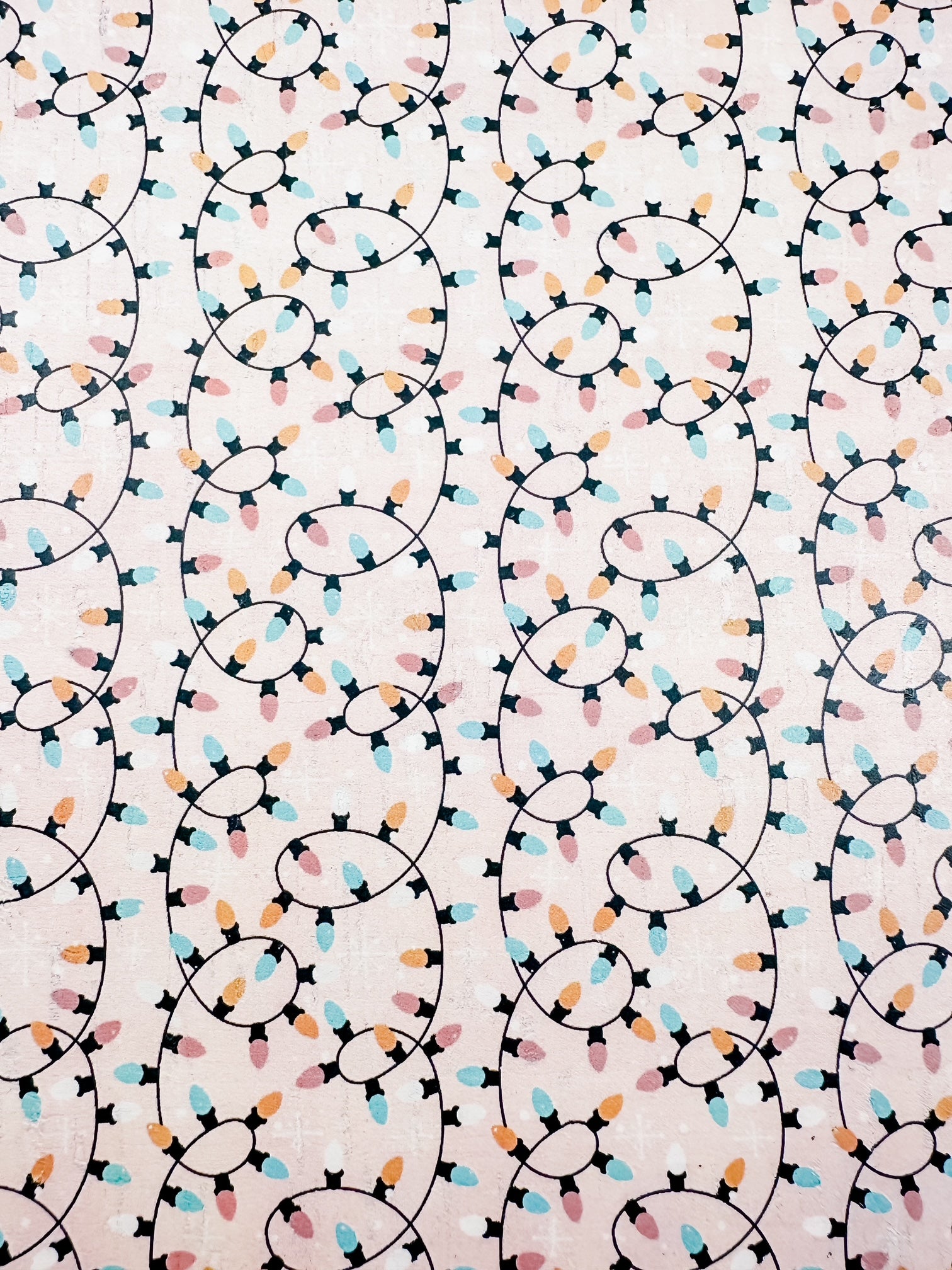 Close-up of blush cork printed with looping strings of pastel Christmas lights