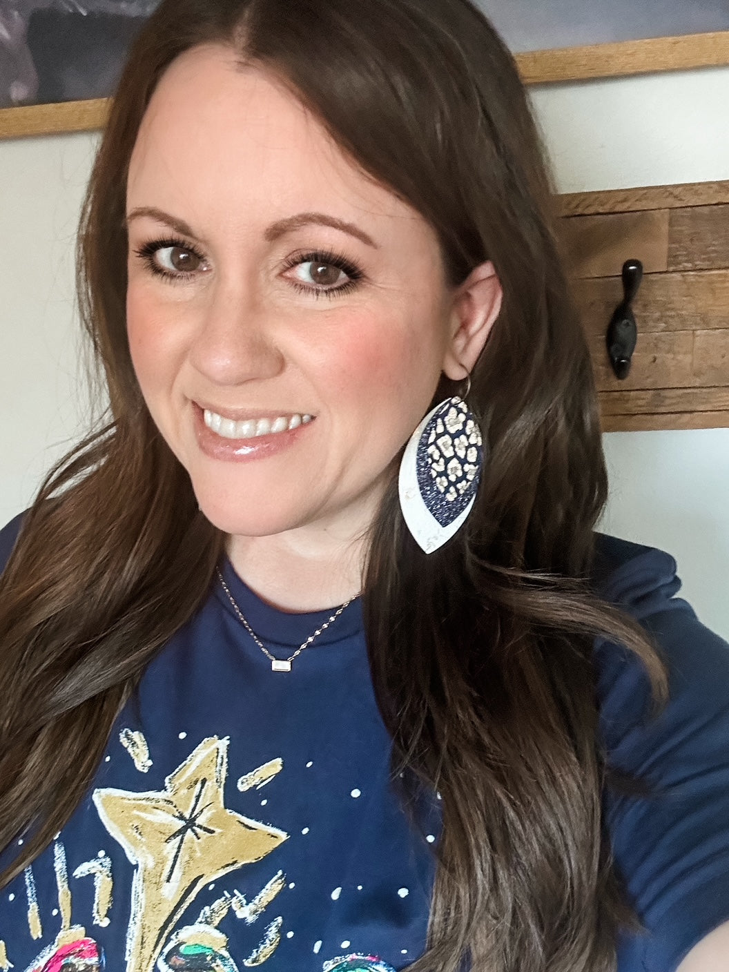 Woman wearing layered navy and gold leather earrings with white distressed base and gold leopard print top layer, styled with a navy tee featuring a gold star design.