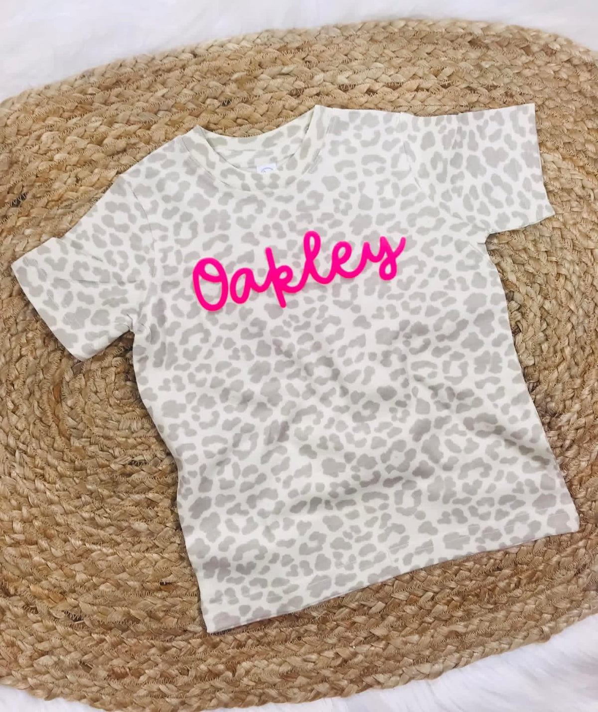 Leopard print Wild Script Tee laid flat on a textured neutral surface with pink script lettering across the front.