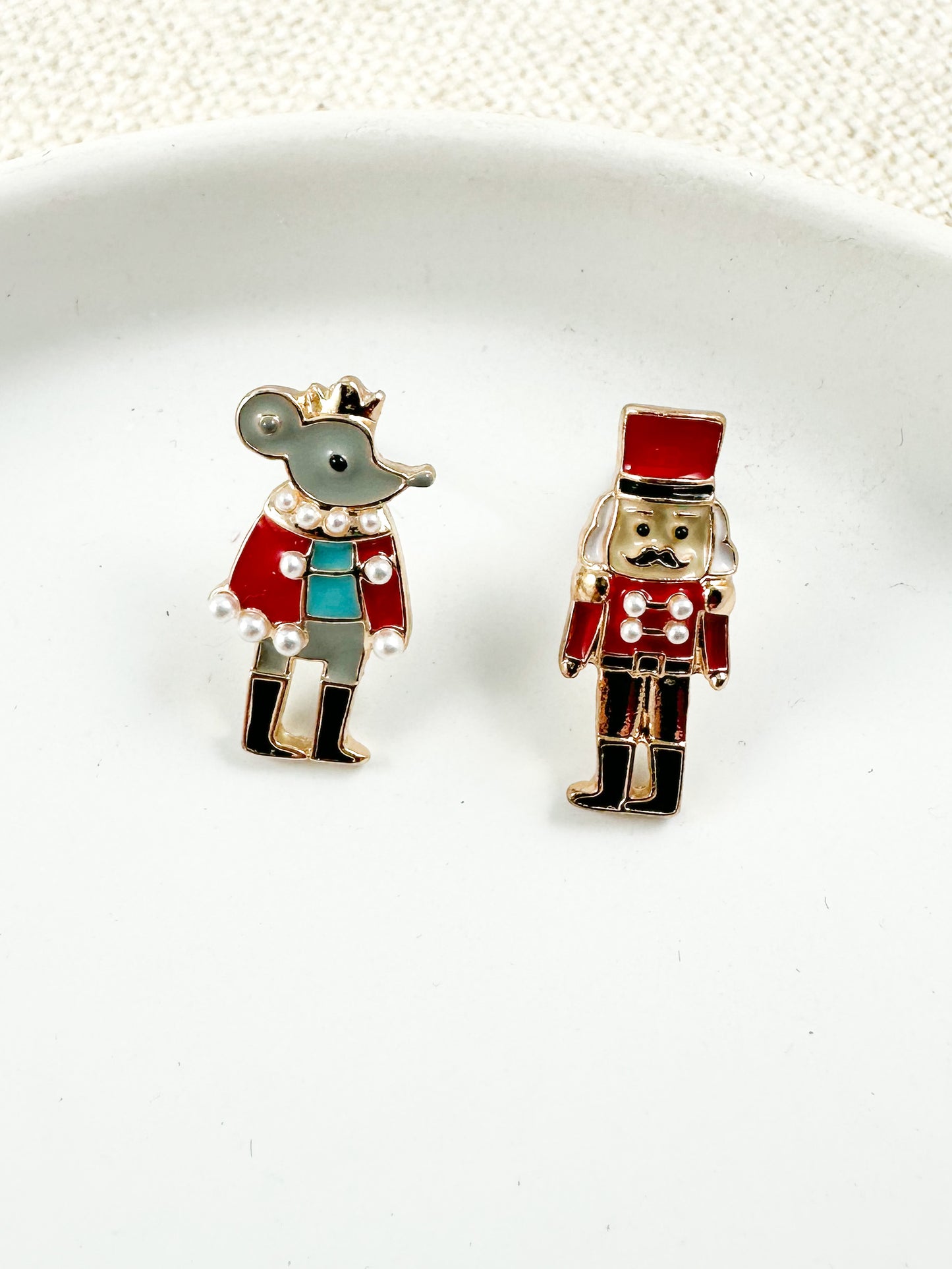 nutcracker and mouse mismatched Christmas stud earrings with enamel and pearl accents on a white dish