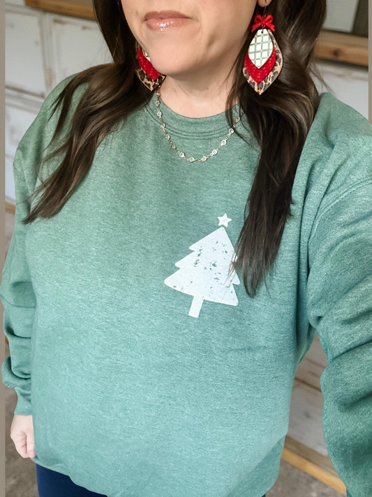 Woman wearing Evergreen Season Sweatshirt in heather forest green with white distressed Christmas tree graphic, cozy unisex crewneck holiday sweatshirt styled with red bow earrings