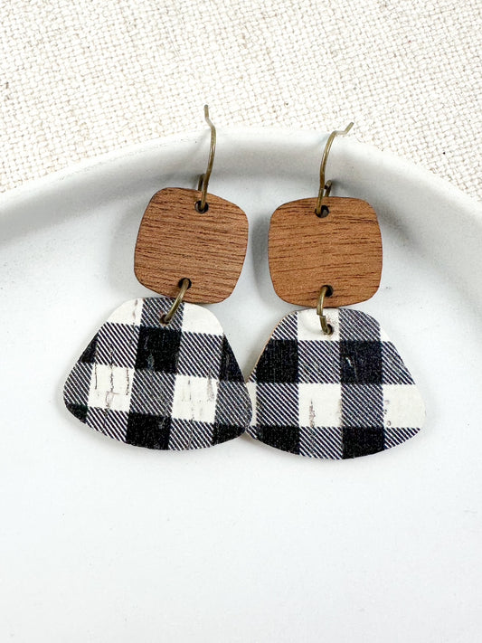 Handmade earrings with wood square tops and black-and-white plaid cork leather bottoms, displayed on a white ceramic dish with a neutral fabric background.