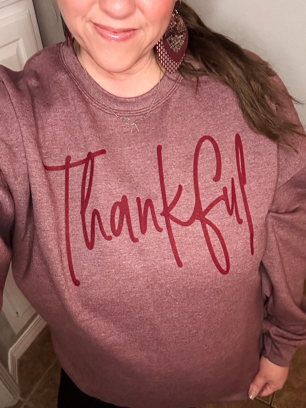 Close-up of woman wearing a heather maroon “Thankful” sweatshirt with deep red lettering, styled casually with statement earrings.