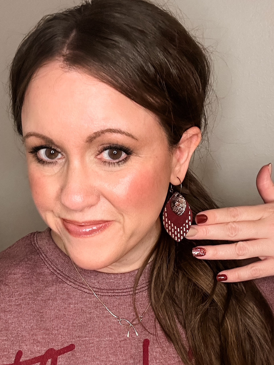 Woman wearing maroon layered leather earrings with gold and snake print details, styled with matching maroon nails and a heather maroon “Thankful” sweatshirt.