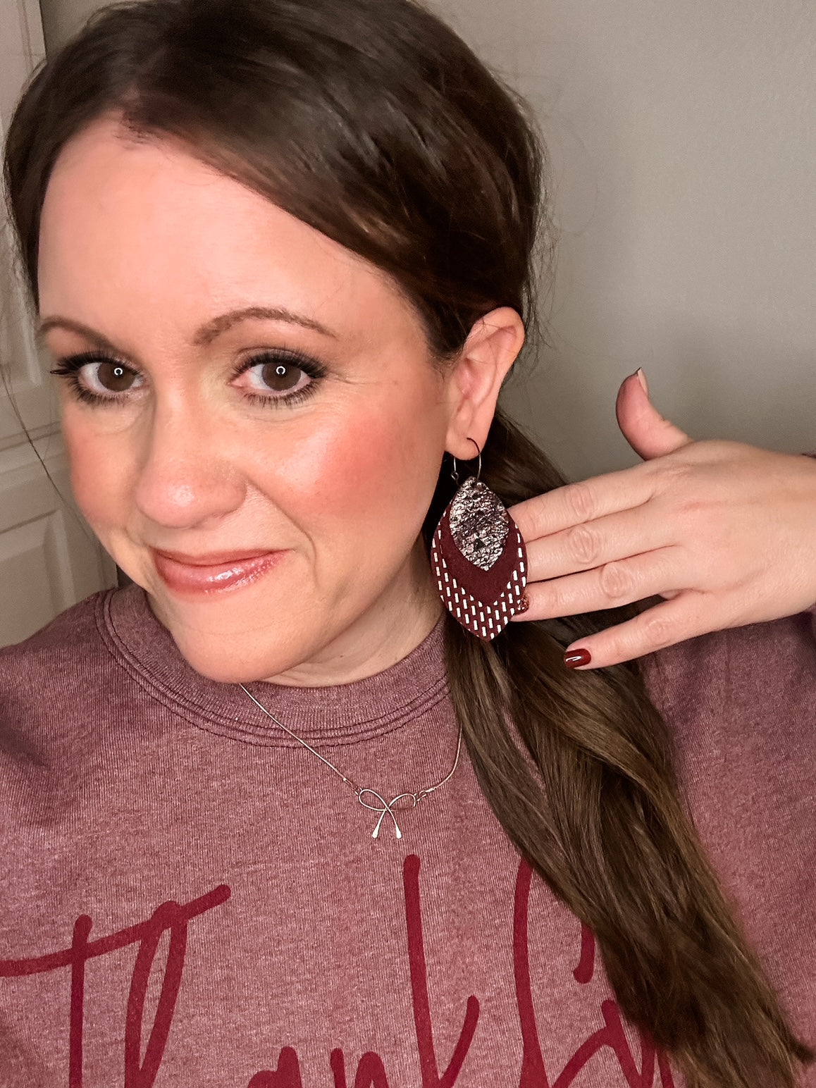 Woman wearing maroon layered leather earrings with gold and snake print details, styled with matching maroon nails and a heather maroon “Thankful” sweatshirt.