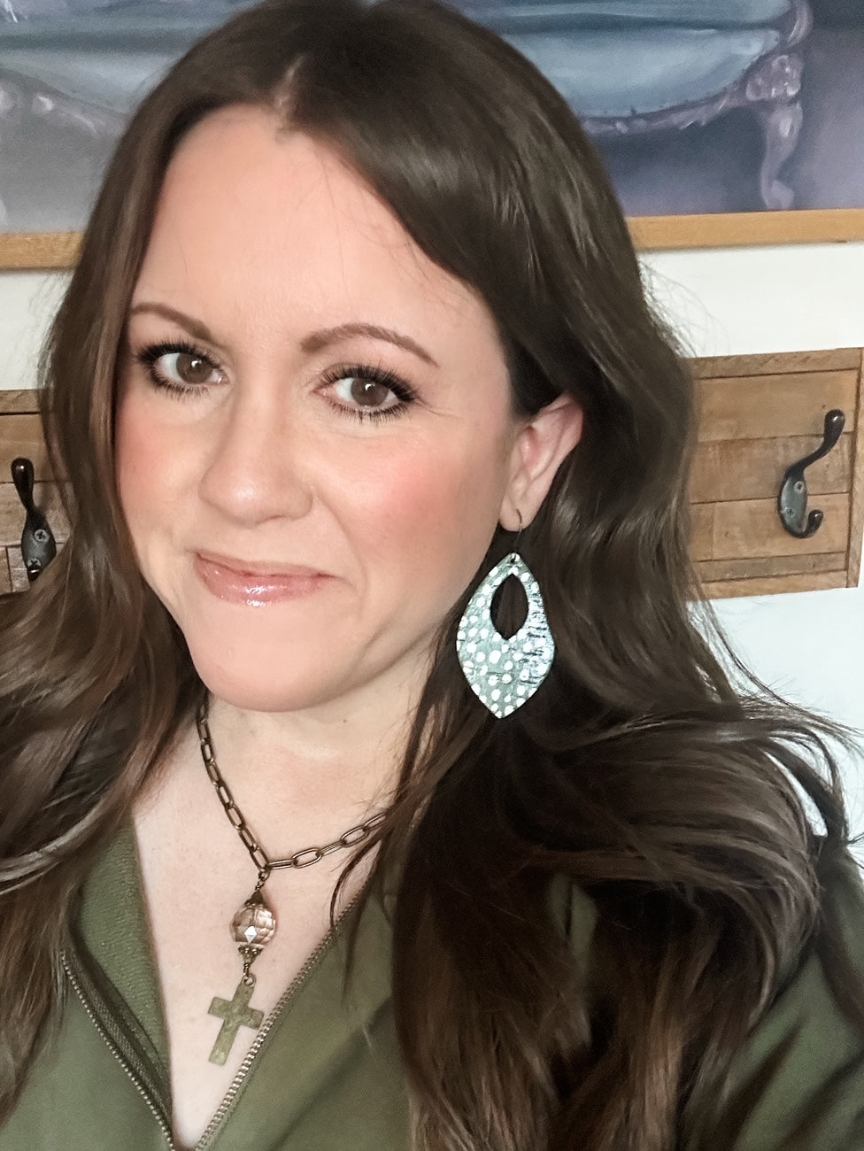 Close-up of a woman wearing large leather Magnolia earrings with a teardrop cutout design and olive green and white polka-dot pattern.