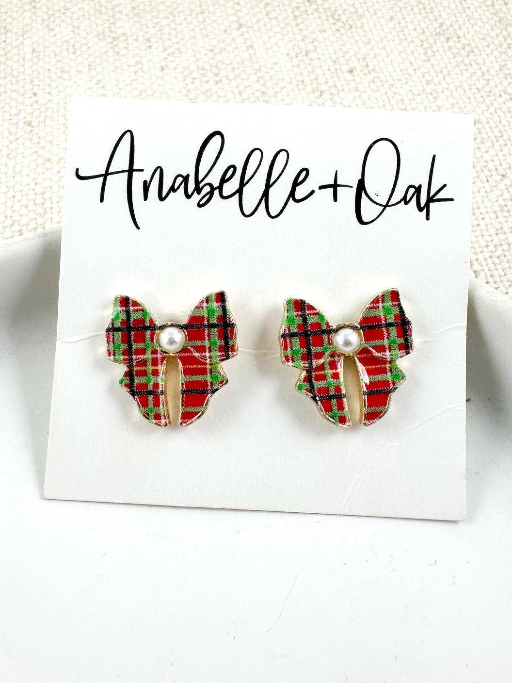Bow-shaped stud earrings in red and green plaid with a pearl center on a light background.