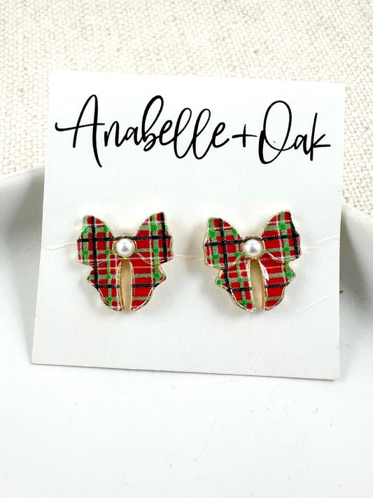 Bow-shaped stud earrings in red and green plaid with a pearl center on a light background.