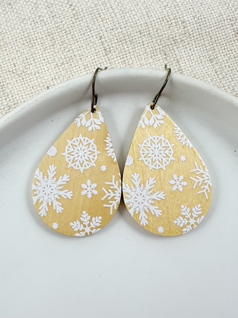 Lightweight wooden teardrop earrings with white snowflake designs on a warm gold background.