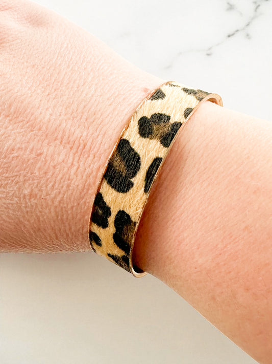 Animal print gold cuff bracelet shown on wrist, featuring soft textured finish and classic leopard-style pattern