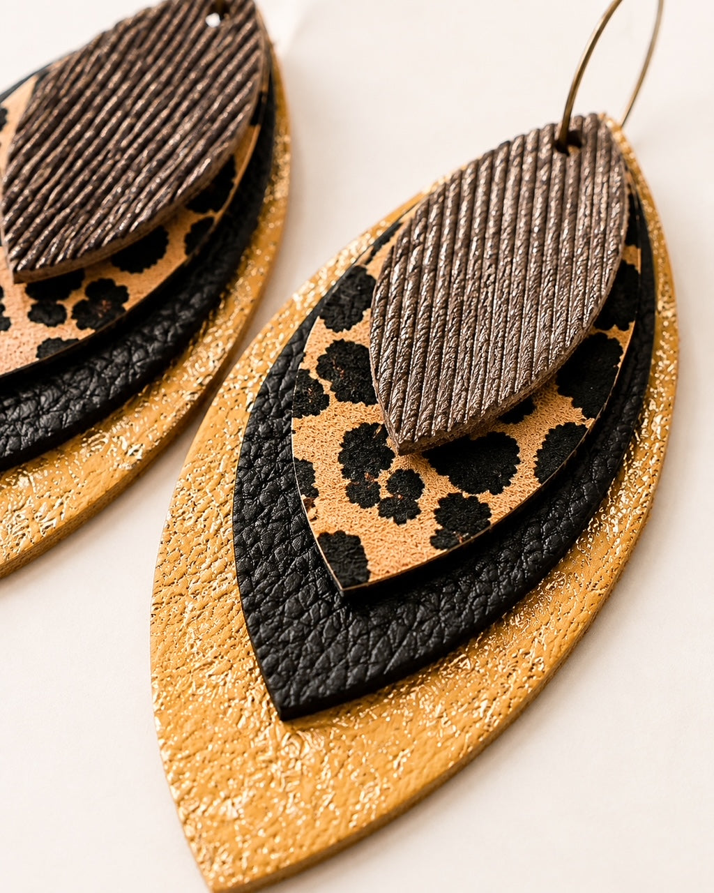 Close-up of layered earrings showing textured brown leather, leopard print, pebbled black leather and metallic gold finish.
